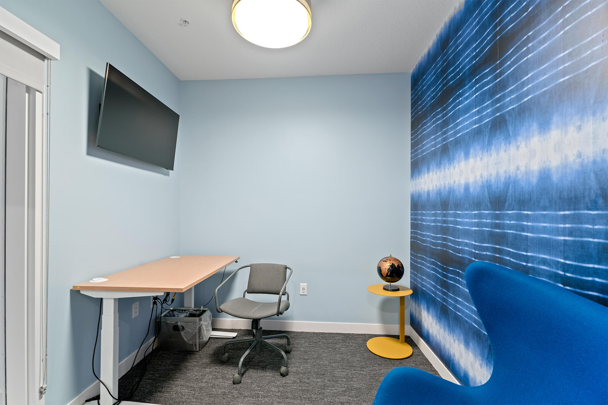 Private office room with desk, chair, mounted TV, and modern blue wall art