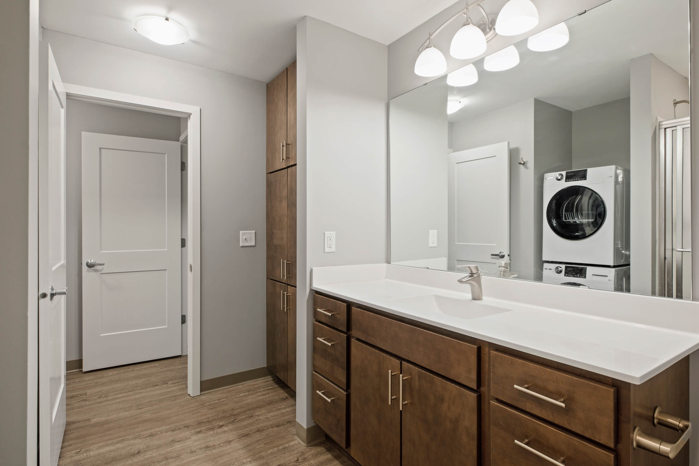 Bathroom with wood vanity and stacked laundry in mirror reflection