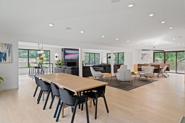 Open-concept lounge with dining table, seating areas, and large windows overlooking greenery
