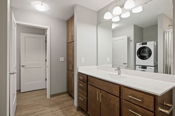 Bathroom with wood vanity and stacked laundry in mirror reflection